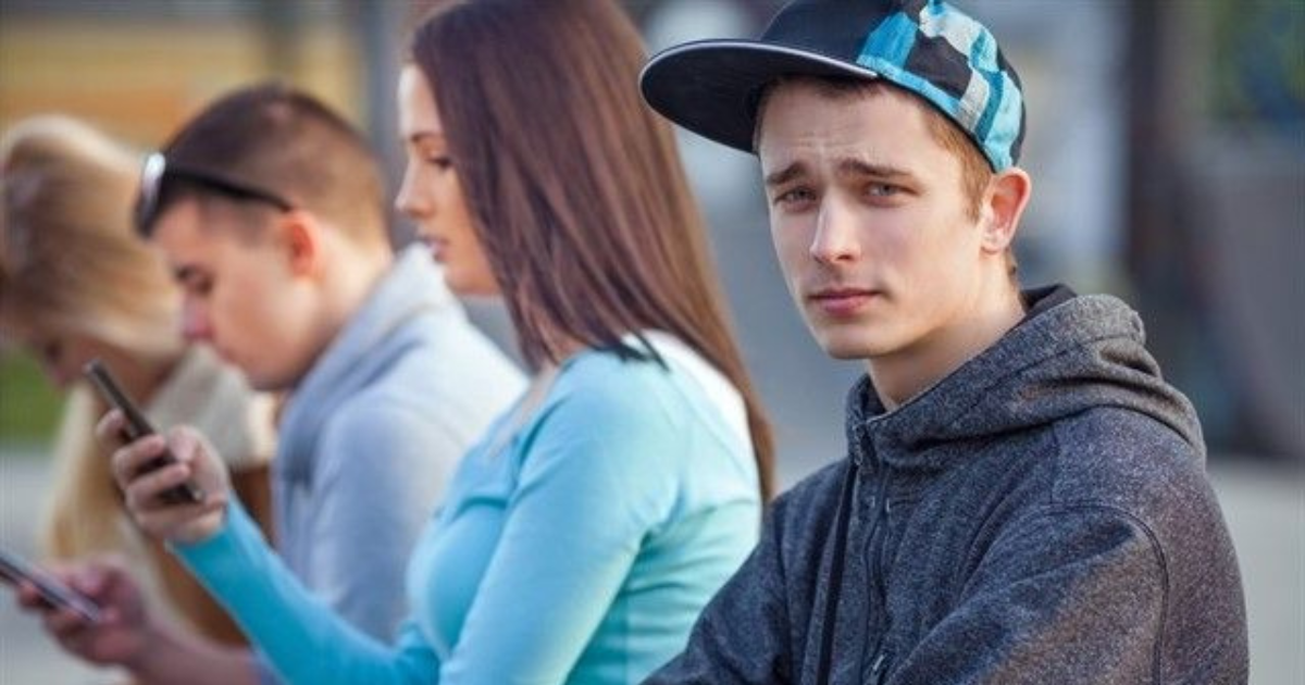 Un chico joven mirando a cámara, mientras otras tres personas a su alrededor están absortas mirando sus teléfonos móviles.