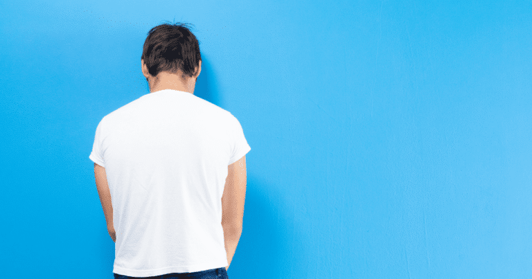 Un hombre joven de espaldas, con la cabeza agachada, sugiriendo tristeza, preocupación o el peso de la ansiedad.