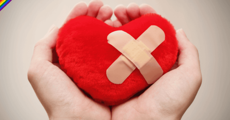 Primer plano de unas manos sosteniendo un corazón de color rojo con una tirita o vendaje, simbolizando el dolor emocional y la sanación.