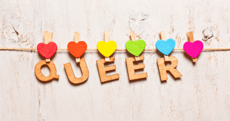 La palabra "QUEER" escrita letra por letra y colgada con pinzas en una cuerda de tender ropa, con corazones de colores LGTBI+ alrededor.