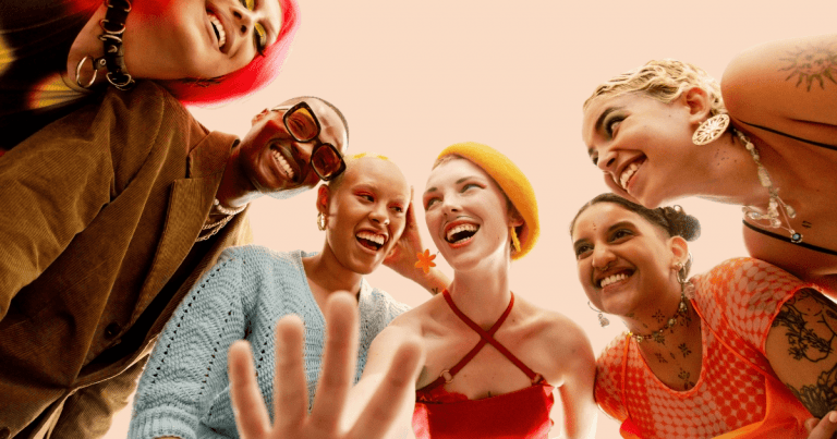 Seis personas jóvenes, diversas en apariencia, sonriendo ampliamente y mirando a cámara, transmitiendo alegría y comunidad.