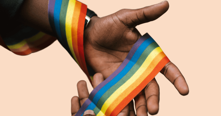 Primer plano de unas manos sosteniendo un lazo con los colores del arcoíris LGTBI+, simbolizando apoyo y concienciación.
