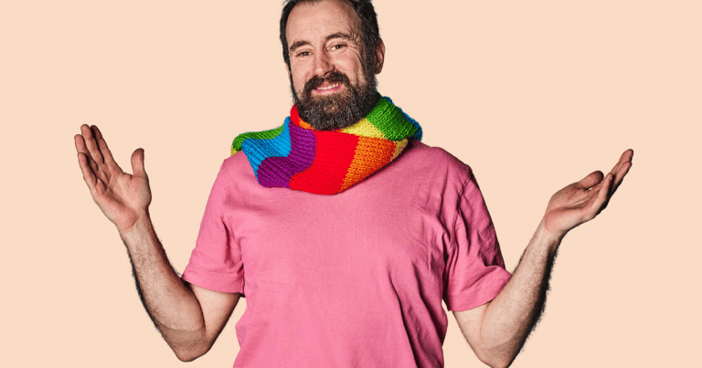 Un hombre sonriente con una bufanda LGTBIQA+, mostrando las palmas de sus manos hacia arriba en un gesto de apertura o celebración.