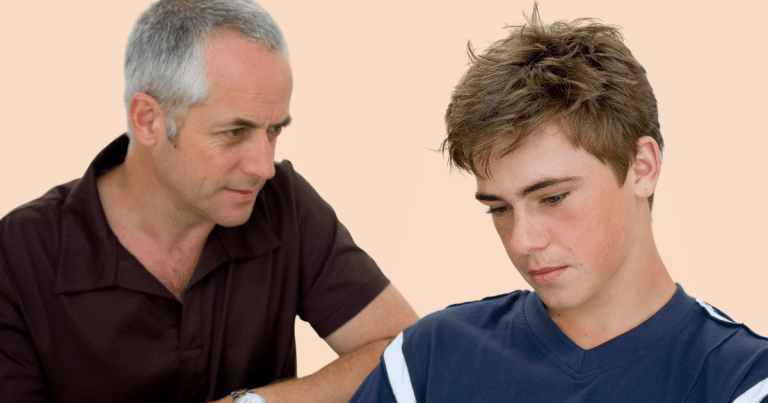 Un padre mirando a su hijo adolescente, quien tiene una expresión triste, simbolizando los desafíos en la aceptación familiar LGTBIQ+.