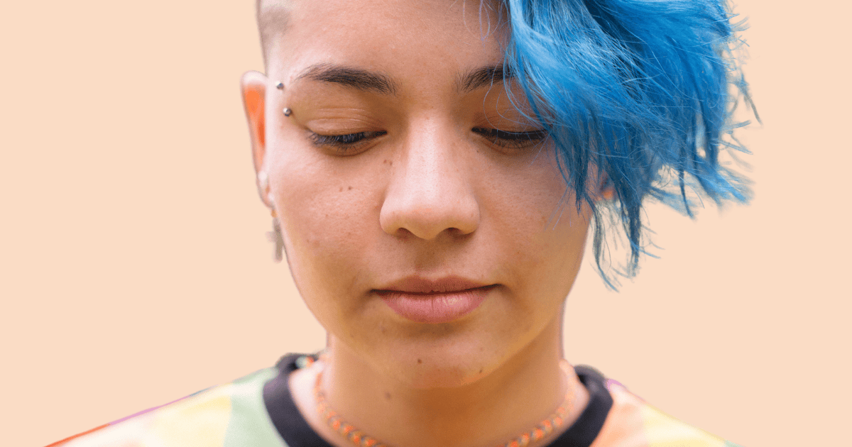 Una chica adolescente con cabello azul intenso, en un plano corto, mirando hacia abajo con expresión pensativa o de preocupación.
