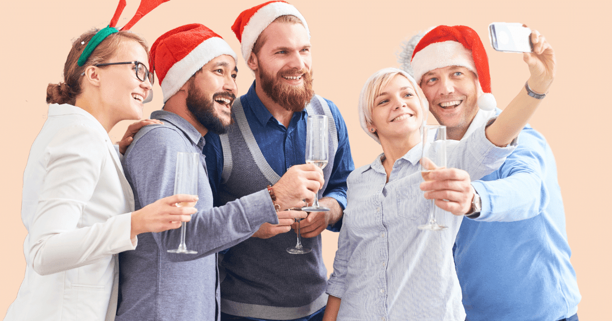 Cinco personas diversas con gorros navideños, sonriendo y haciéndose un selfie, celebrando en un ambiente de empresa inclusivo.