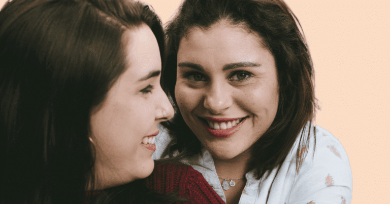 Dos mujeres sonriendo en un plano cercano; una mira a la otra con cariño, mientras la otra sonríe a cámara.