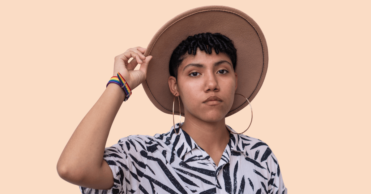 Un hombre queer con un sombrero, mirando seriamente a cámara, sugiriendo un sentimiento de introspección o preocupación.