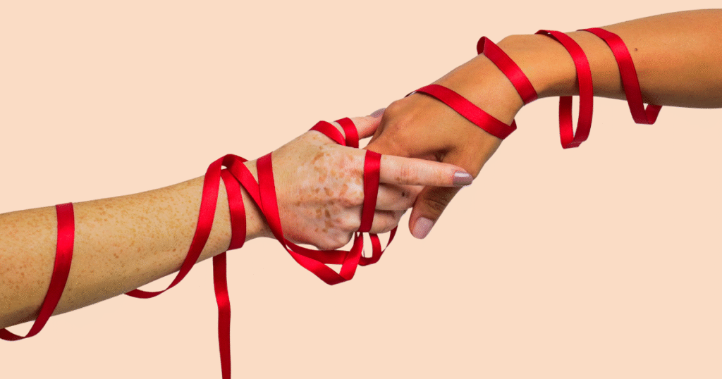 Dos manos entrelazando el lazo rojo, símbolo de la lucha contra el VIH/SIDA y la solidaridad.
